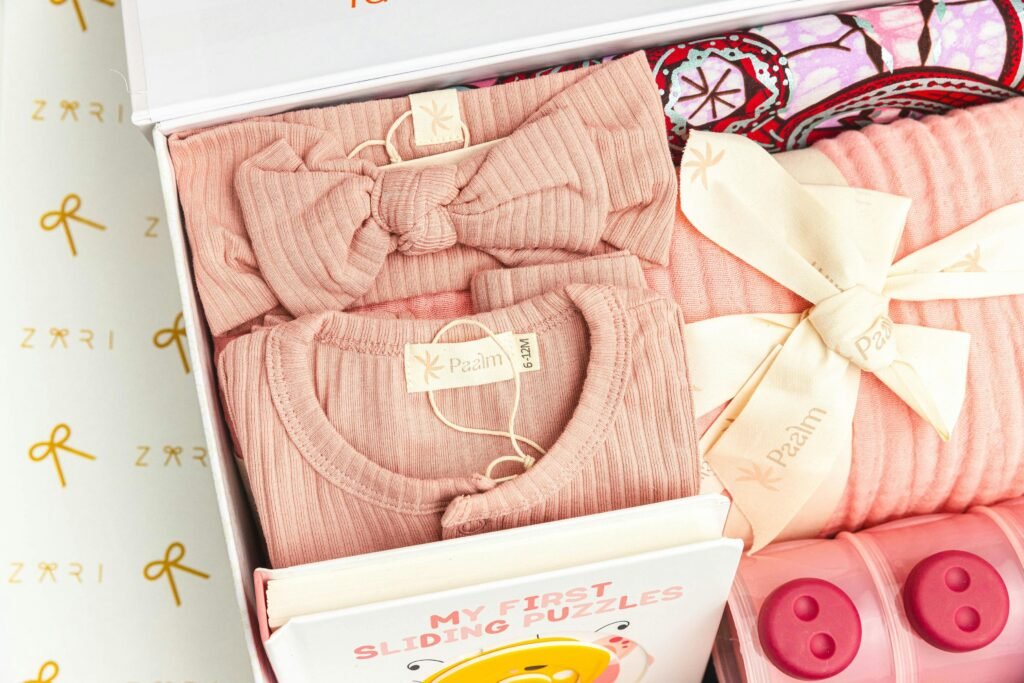 Adorable pink baby clothing set with tied bows and a puzzle book in a gift box.
